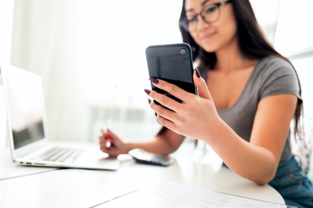 Asian woman using smartphone app and laptop for calaulating home budget finance taxes