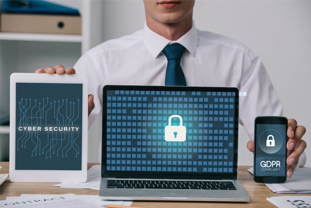 cropped shot of businessman showing laptop, tablet and smartphone with gdpr and cyber security signs